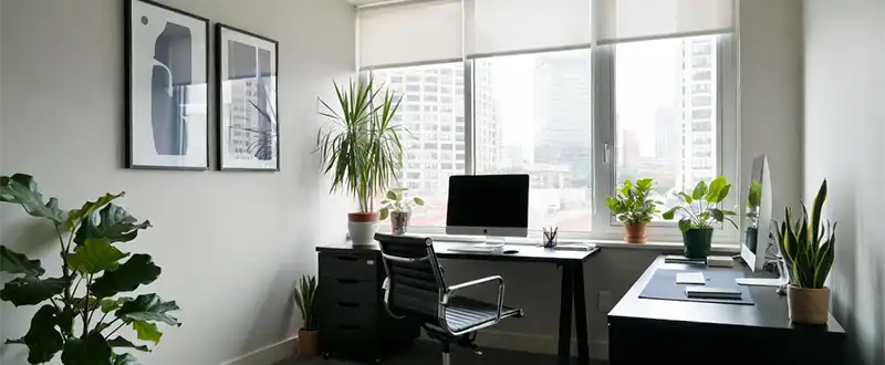 Escritório iluminado com mesas, computadores e plantas junto às janelas